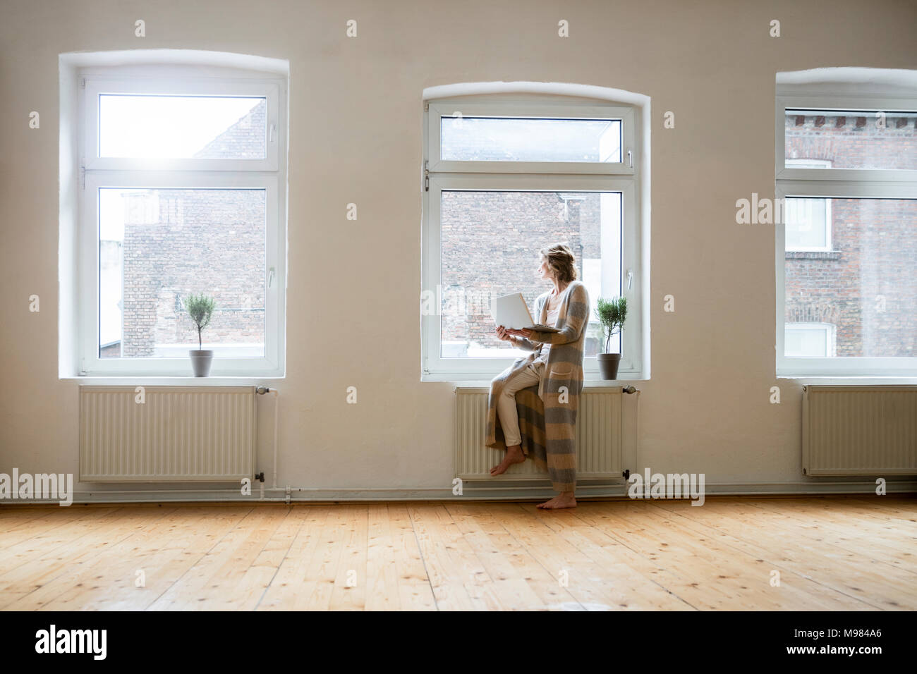 Reife Frau im leeren Raum holding Laptop am Fenster Stockfoto