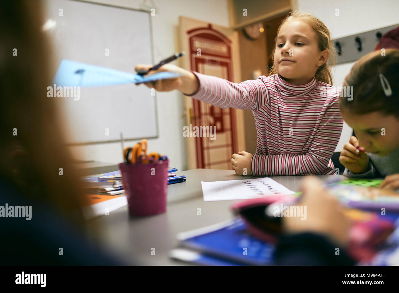 Schoolgirlhanding über Blatt Papier zu Mitschüler in der Klasse Stockfoto