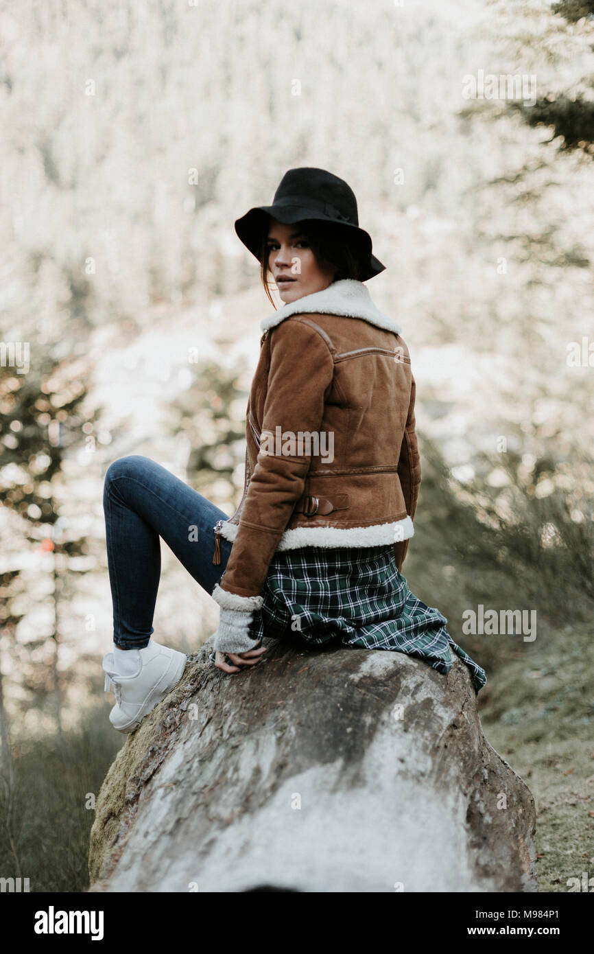 Porträt der jungen Frau sitzt auf einem Baumstamm in der Natur Stockfoto