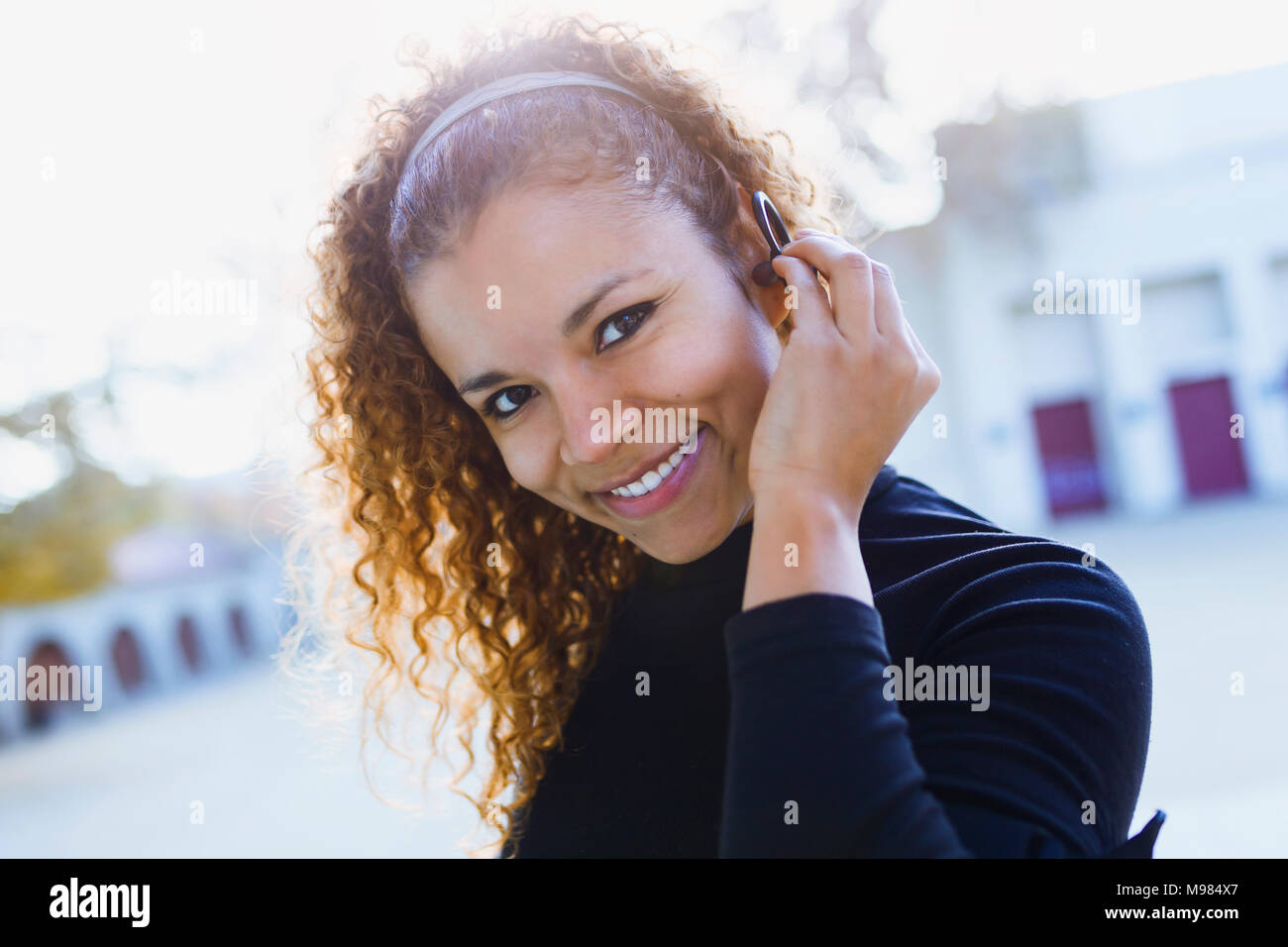 Portrait von lächelnden jungen Frau im Freien auf Ohrhörer Stockfoto