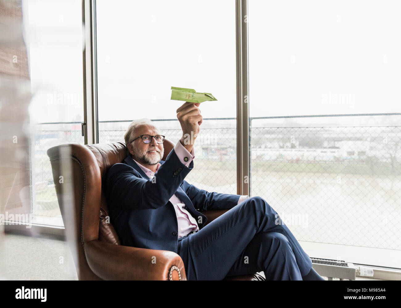 Lächelnd reife Geschäftsmann sitzen in Leder Sessel holding Paper Plane Stockfoto