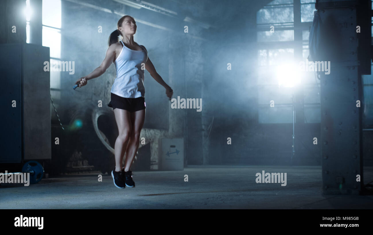 Athletische schöne Frau Übungen mit Jump/Springseil in ein Fitnessstudio. Sie ist in Schweiß von der intensiven Cross Fitness Training abgedeckt. Dunkle Atmosphäre Stockfoto