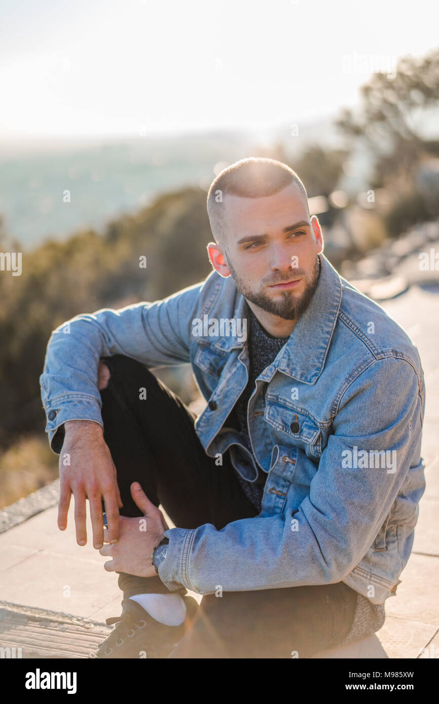 Ernsthafte junge Mann sitzt auf einer Wand Stockfoto