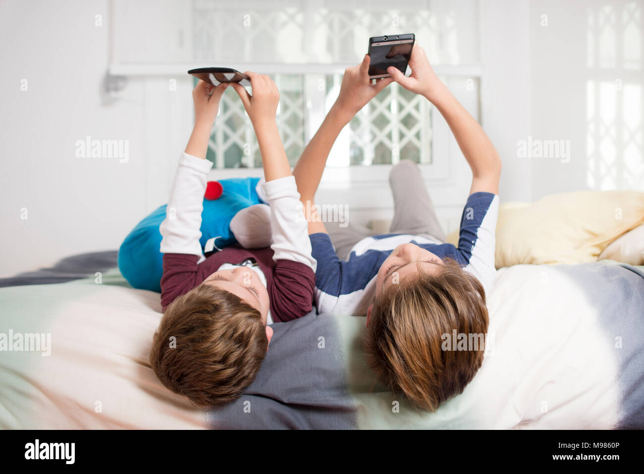 Zwei Jungen liegend auf Bett zu Hause über Mobiltelefone Stockfoto