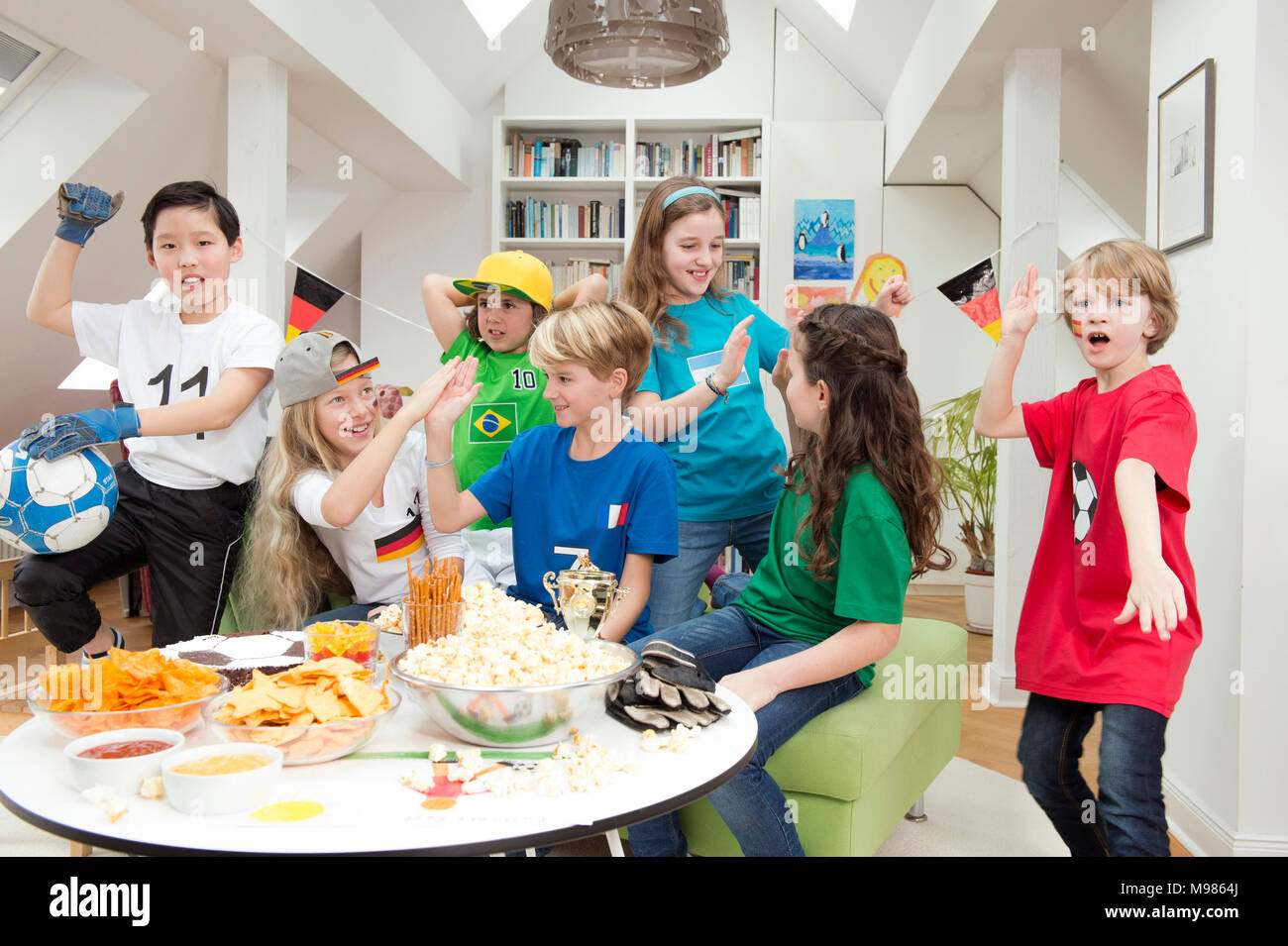 Gruppe von Kindern beobachten Fußball-WM mit einem Tisch voller Süßigkeiten und Snacks Stockfoto