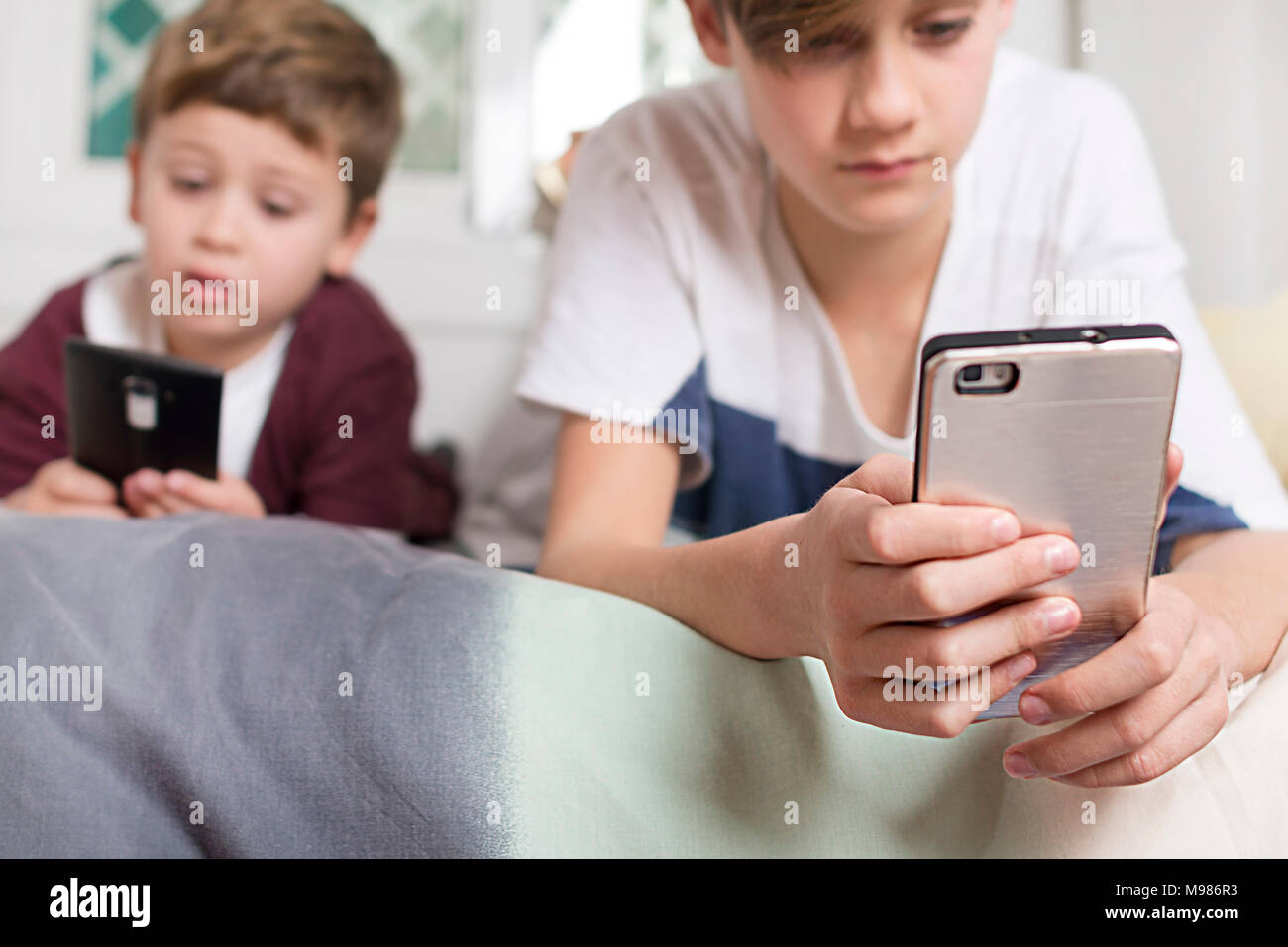 Zwei Jungen liegend auf Bett zu Hause über Mobiltelefone Stockfoto