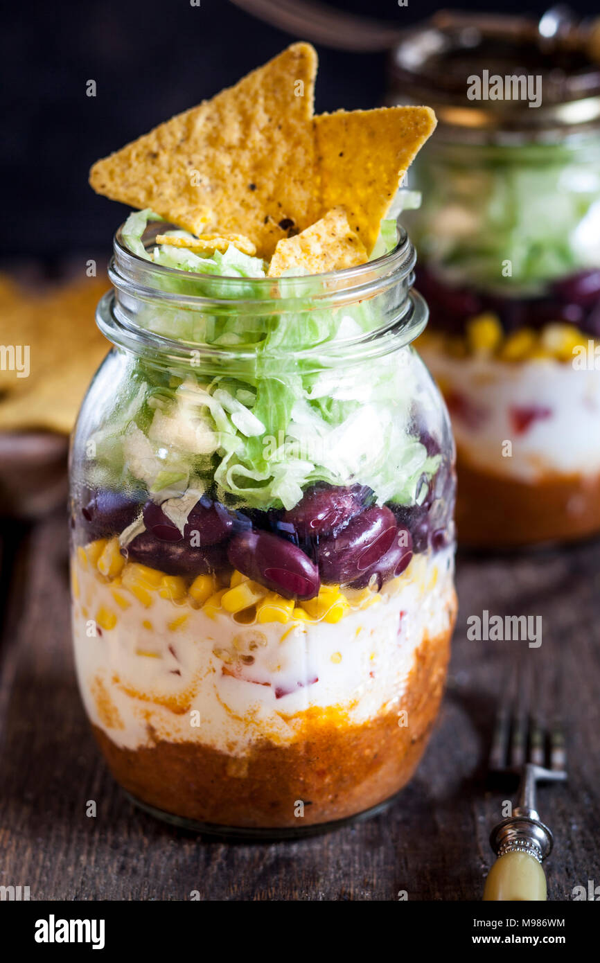Taco Salat, Chili con Carne, saure Sahne, Mais, Bohnen, Eisbergsalat in einem Glas, Nacho Chips Stockfoto