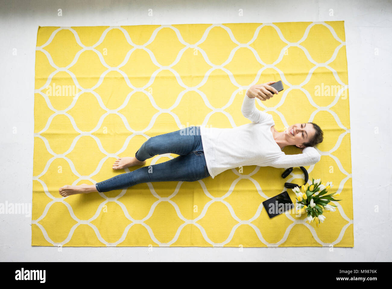 Lächelnde Frau mit Handy liegen auf Teppich mit Bündel Tulpen Stockfoto