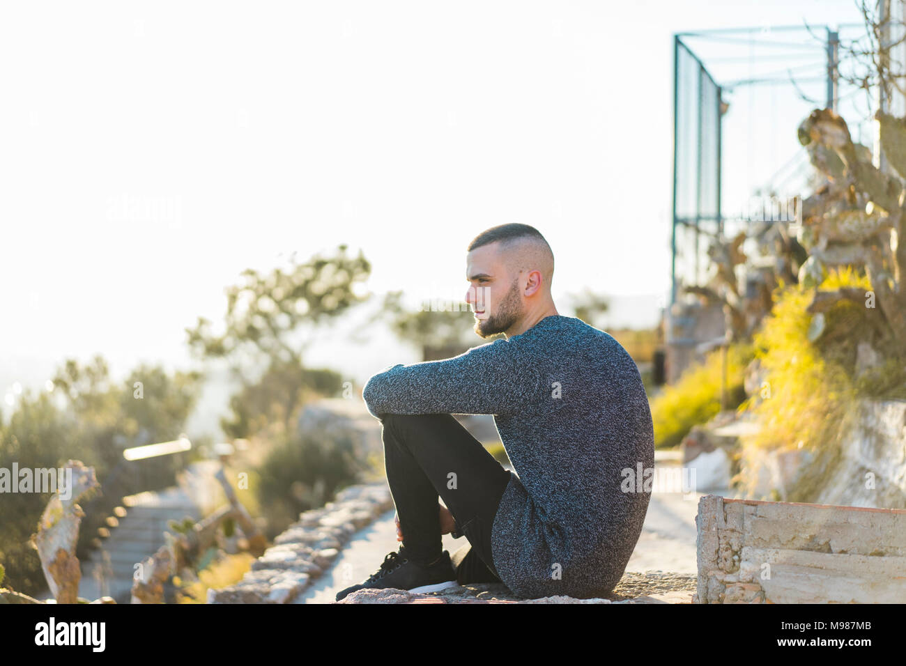 Ernsthafte junge Mann sitzt auf einer Wand Stockfoto