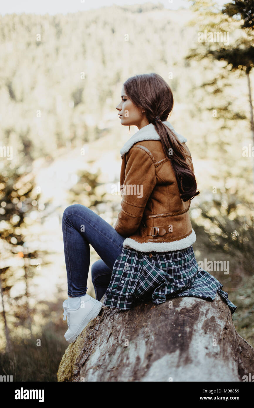 Junge Frau sitzt auf einem Baumstamm in der Natur Stockfoto