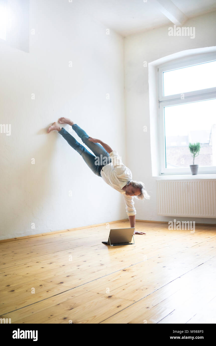 Reifer Mann macht einen Handstand auf Fußboden im leeren Raum auf der Suche nach Tablet Stockfoto