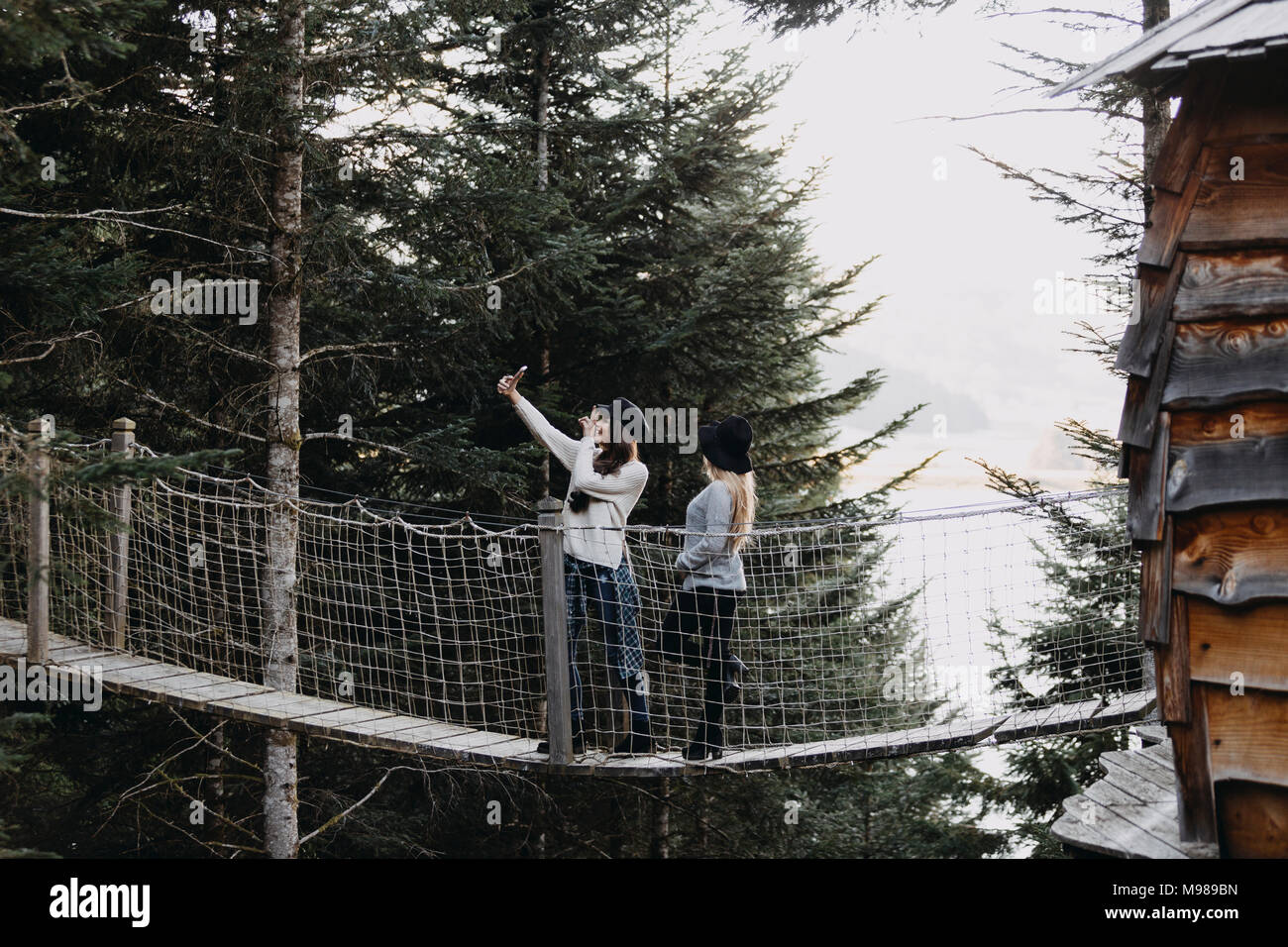 Zwei junge Frauen auf einer Hängebrücke im Baumhaus im Wald unter einem selfie Stockfoto