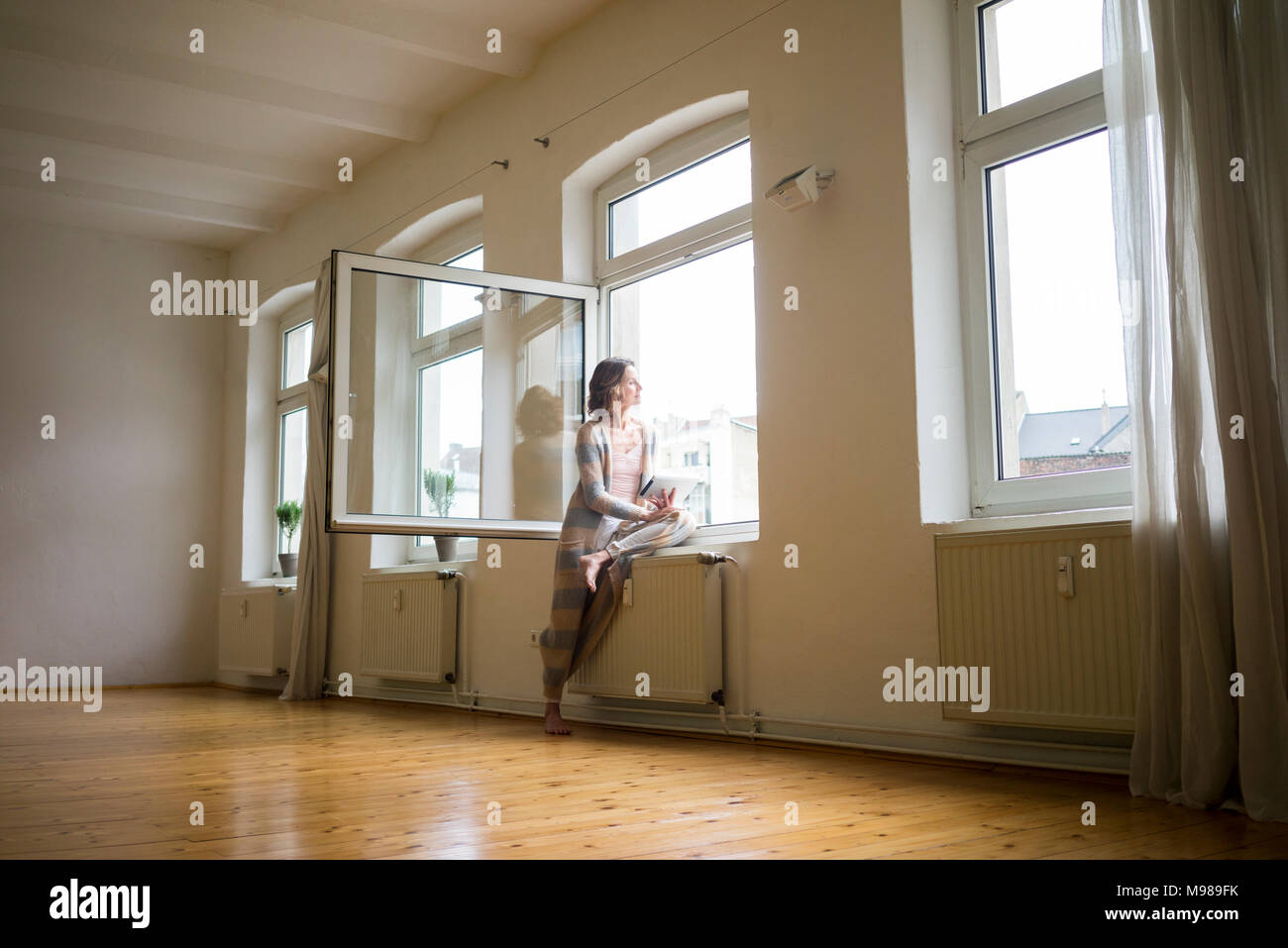 Reife Frau im leeren Raum Holding tablet Blick aus Fenster Stockfoto