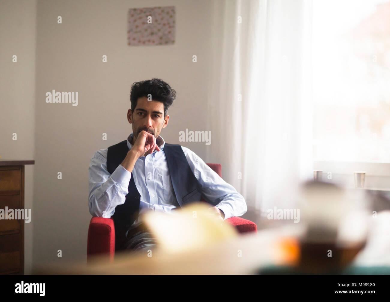 Portrait von nachdenklicher Mann, der auf einem Sessel zu Hause sitzen Stockfoto