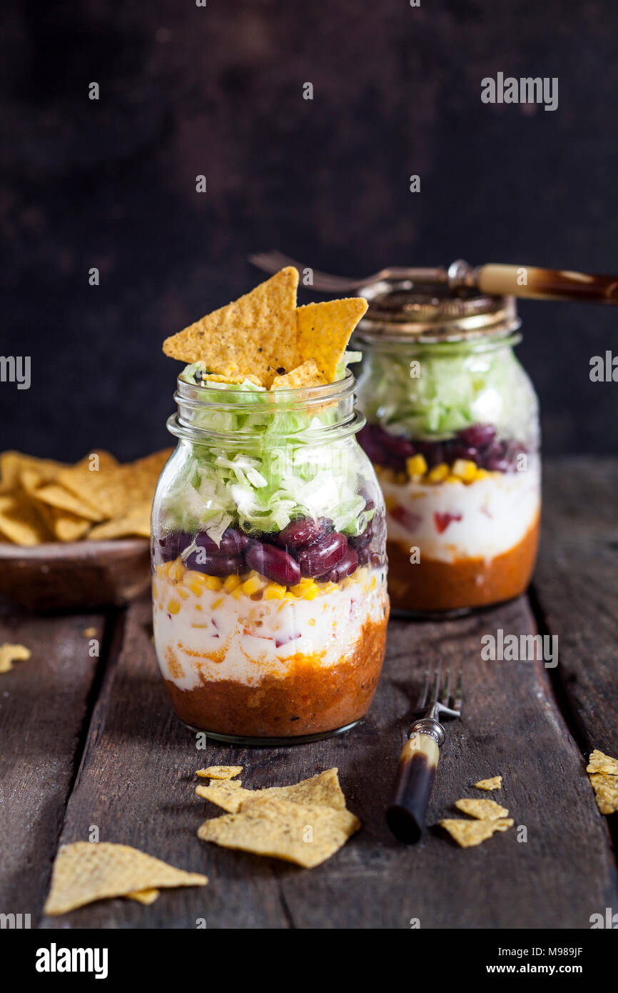 Taco Salat, Chili con Carne, saure Sahne, Mais, Bohnen, Eisbergsalat in einem Glas, Nacho Chips Stockfoto