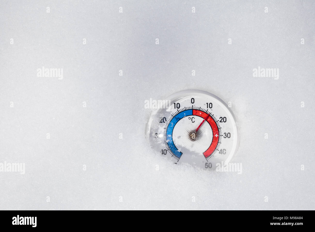 Thermometer mit Celsius im schmelzenden Schnee mit plus 12 Grad Celsius warmen Wetter im Frühling oder die globale Erwärmung Konzept Stockfoto