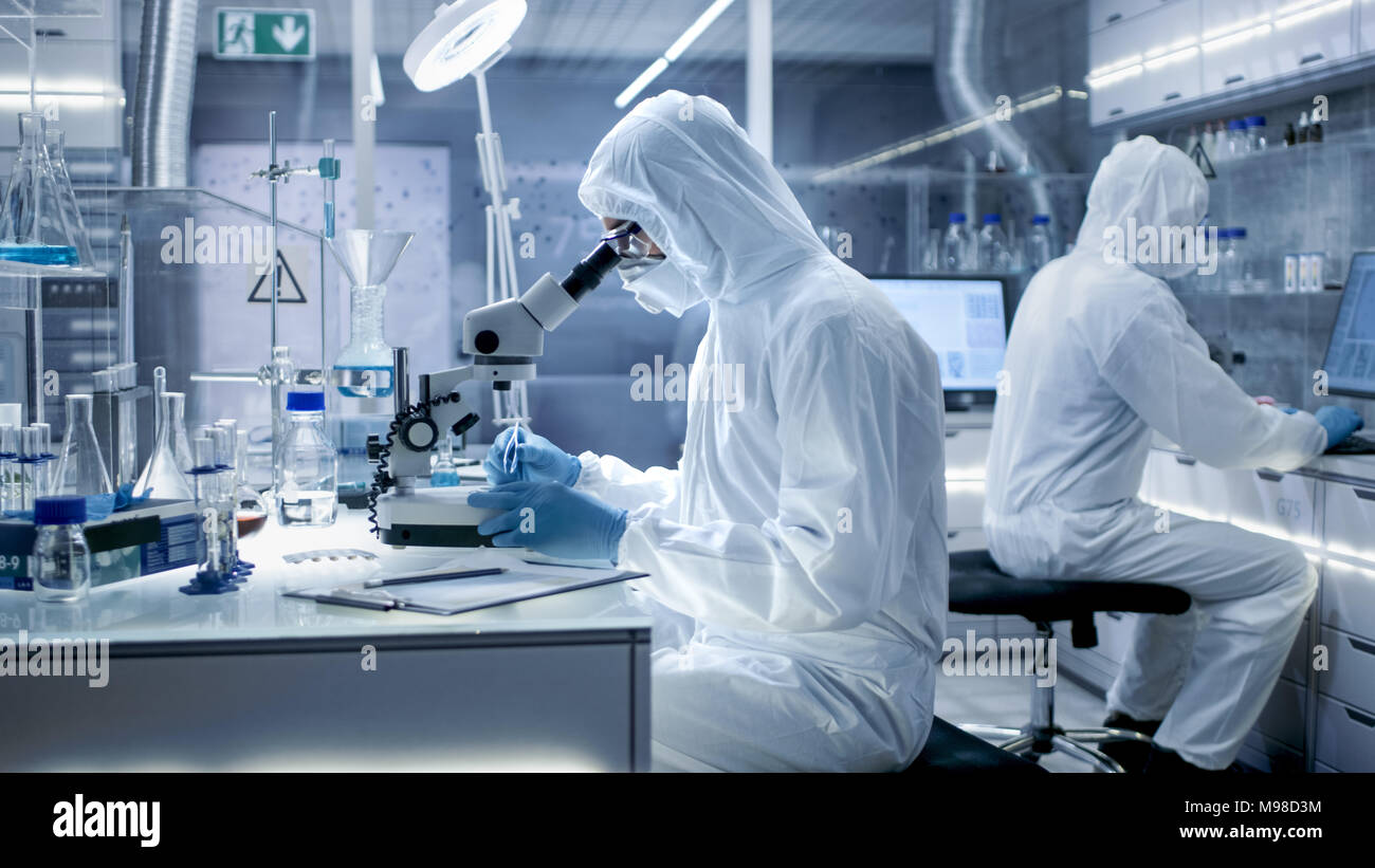 In einem sicheren Hohe Labor Wissenschaftler in einem Overall, die Durchführung einer Forschung. Biologe passt die Proben in eine Petrischale mit einer Zange und untersucht Stockfoto