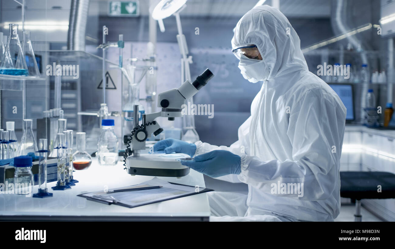 In einem sicheren Hohe Labor Wissenschaftler in einem Overall, die Durchführung einer Forschung. Biologe passt die Proben in eine Petrischale mit einer Zange und untersucht Stockfoto