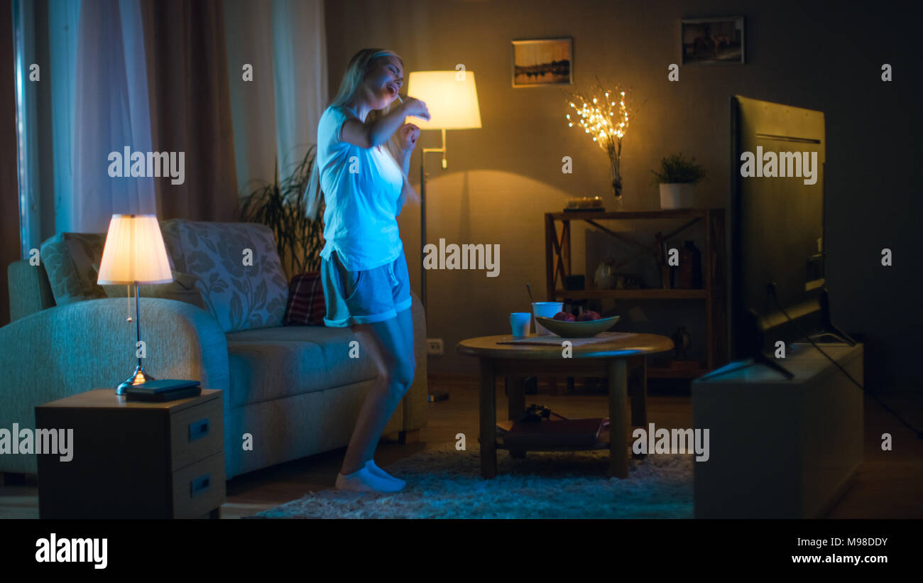 Am Abend schöne Frau glücklich Tänze in Ihrem Wohnzimmer, während Sie fernsehen, auch Sie hält Smartphone. Stockfoto