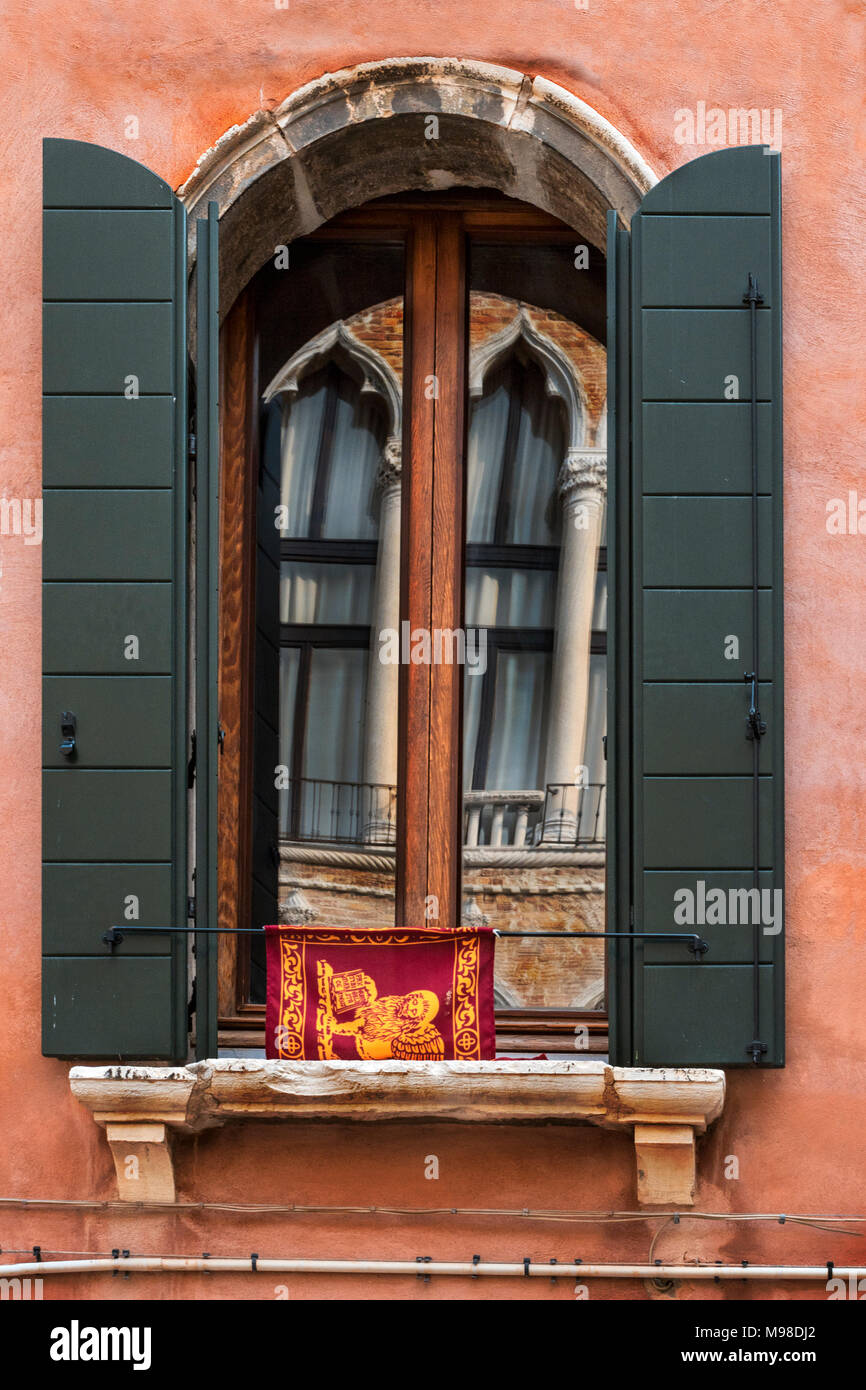 Gestelzt Gotischen lancet Bögen der byzantinischen und maurischen Einfluss mit Spalten in einem Gestelzten arch Fenster mit grünen Fensterläden und Flagge wider Stockfoto