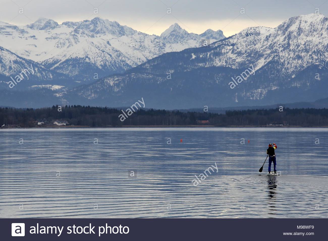 Ein Mann an Bord eines paddle Board macht sich auf den Weg Richtung Alpen am Starnberger See Stockfoto