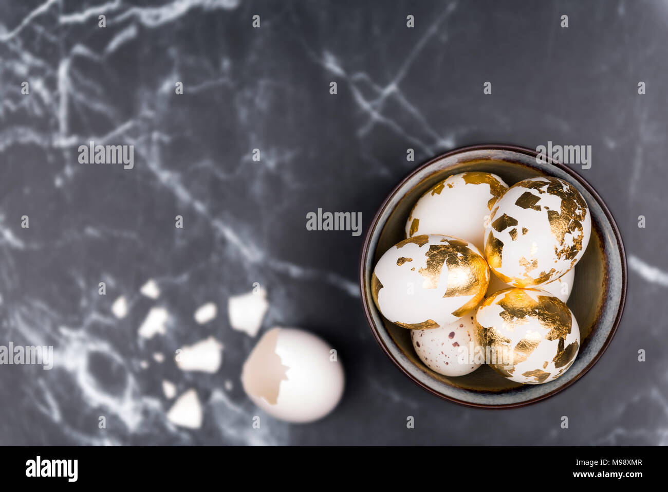 Feminine stilvollen Hintergrund, weiße Eier mit goldene Folie im rustikalen Schüssel eingerichtet, und zerbrochene Eierschale. Platz für Text auf schwarzem Marmor Hintergrund. Stockfoto