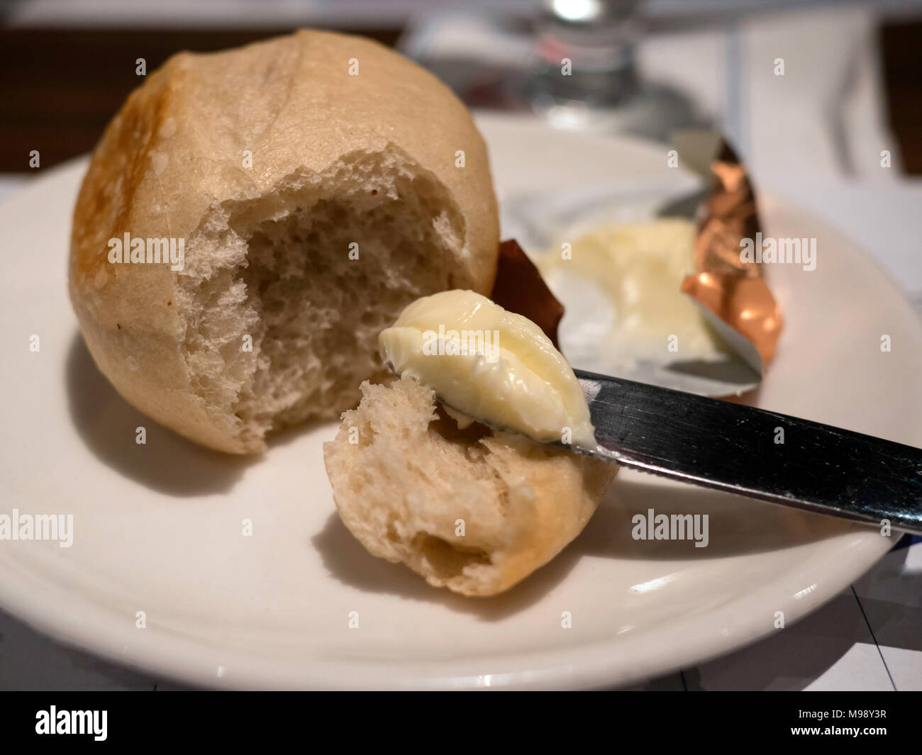 Frisch gebackene Brötchen und Butter auf eine weiße Platte mit einem Messer Stockfoto