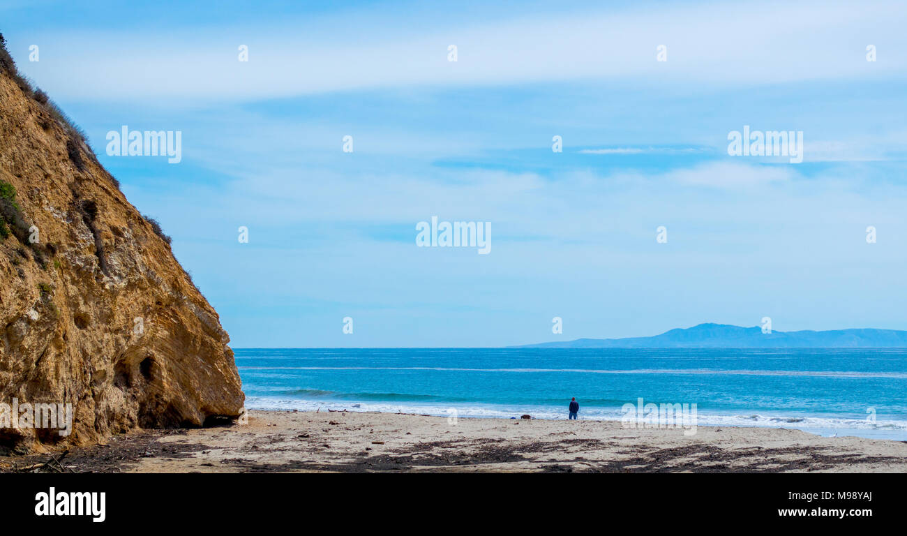 Ein Mann und sein Hund wandern entlang der Sand am Strand von Santa  Barbara, Kalifornien, in der Nähe einer steilen felsigen Hügel mit Anacapa  Island in der Ferne Stockfotografie - Alamy
