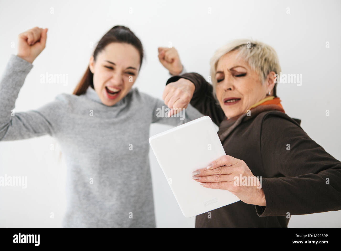 Ein junges Mädchen und einer älteren Frau Blick auf etwas Interessantes auf dem Tablett und zeigen Emotionen. Kommunikation, gemeinsame Freizeitgestaltung von jungen und alten Menschen. Stockfoto