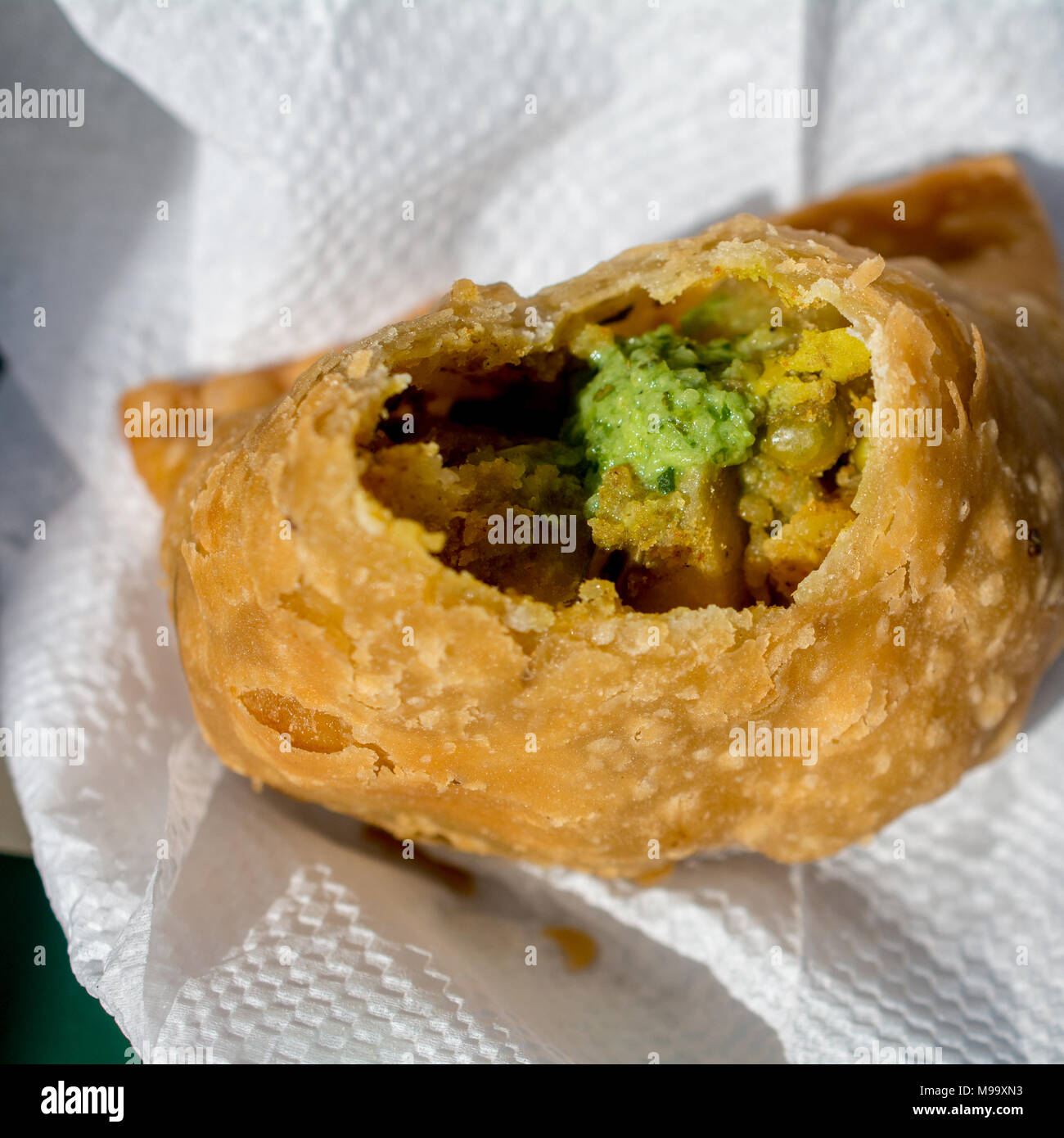 Gebissen die Hälfte gegessen Samosa auf weißen Serviette serviert mit Indischer Koriander Würze zu Ansicht Stockfoto