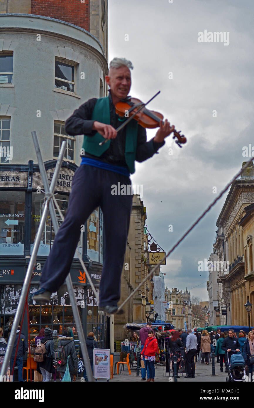 Bristol, UK. 24. März 2018. Ein Nachmittag der Straßenunterhaltung in Wein Straße, Bristol. Eine Performance von slacklining zwischen zwei Pfosten durch die Person spielt eine Violine und gekonnt Balancing beim Gehen auf ein Seil in middair unterbrochen und von Zuschauern verfolgt werden. Robert Timoney/Alamy/live/Aktuelles Stockfoto