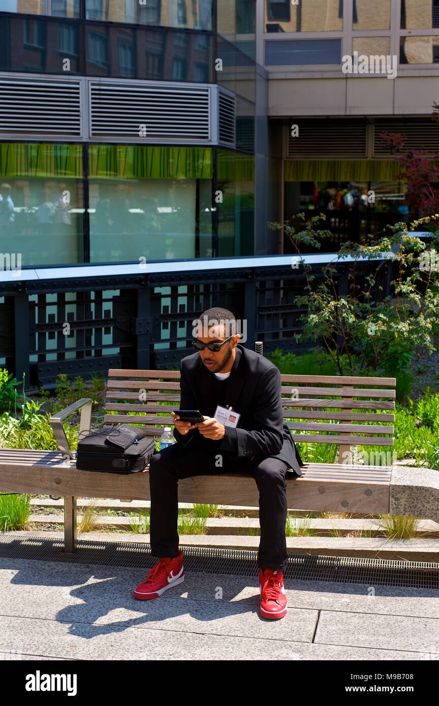 Junger Mann schaut auf sein Handy in roten Schuhen auf der High Line, New York April 2012 Stockfoto
