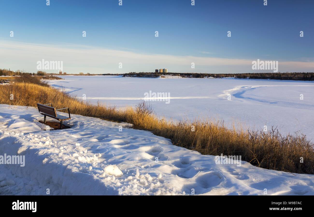 Isolierte Parkbank und Fernen schneebedeckten Glenmore Behälter malerische Landschaft im Süden von Calgary, Alberta auf frühen Frühling sonnigen Nachmittag Stockfoto