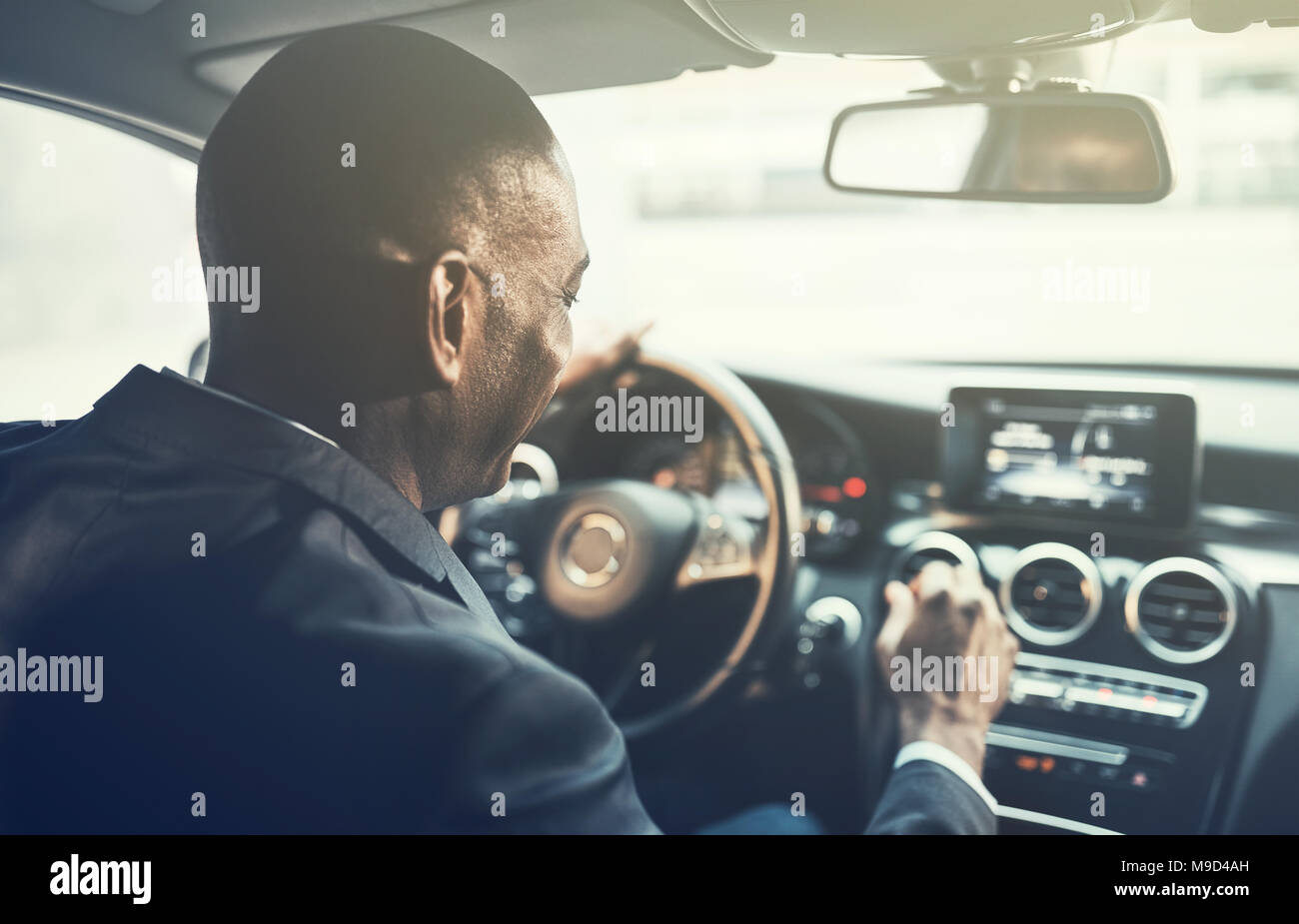 Rückspiegel eines jungen afrikanischen Geschäftsmann ändern Radio Stationen während der morgendlichen Fahrt zum Arbeitsplatz in der Stadt zu arbeiten Stockfoto