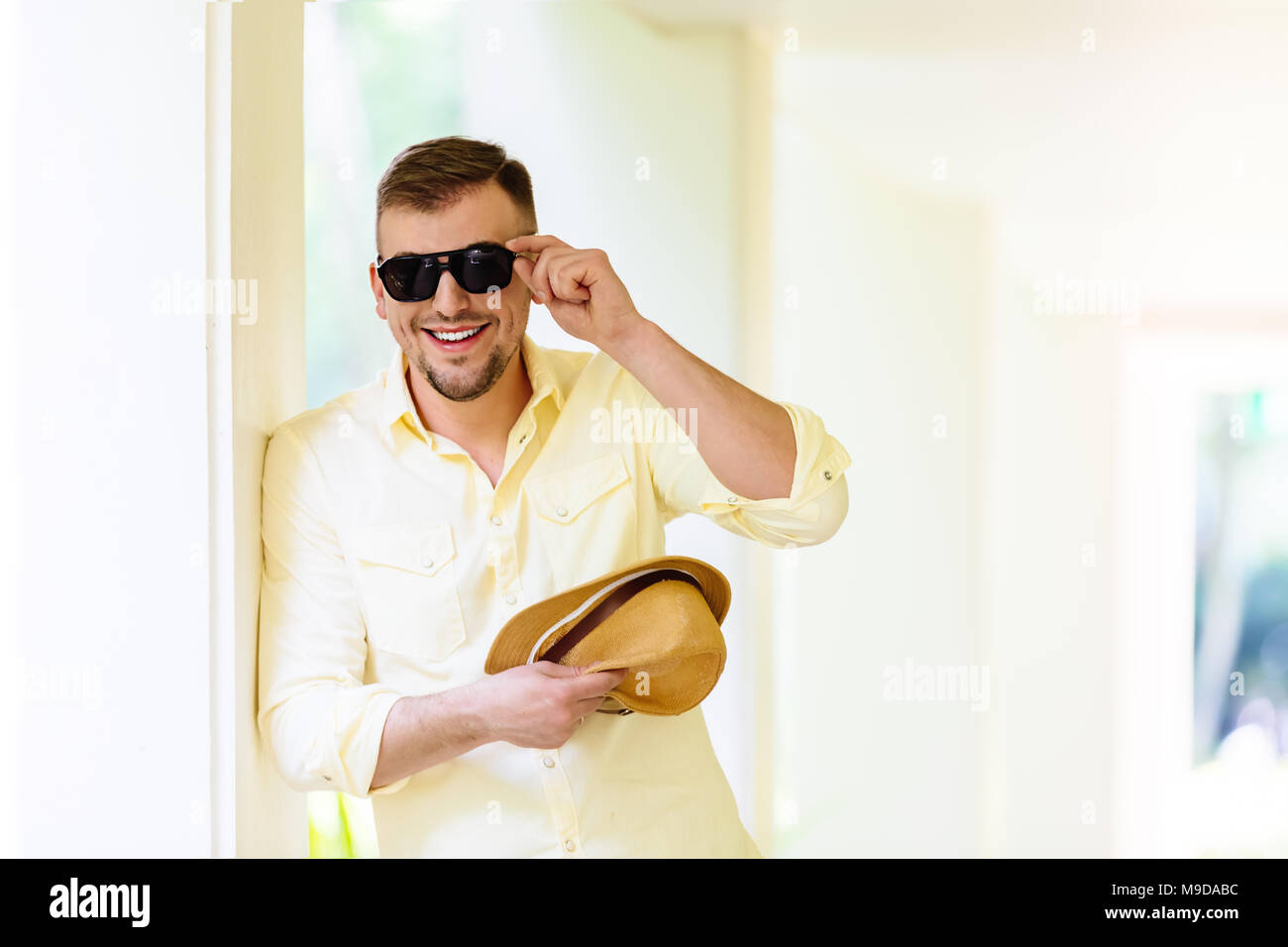 Junger Mann in eine Sonnenbrille tragen gelbe Hut und legere Kleidung Spaß im sonnigen Tag. Tropischen Hintergrund. Stockfoto