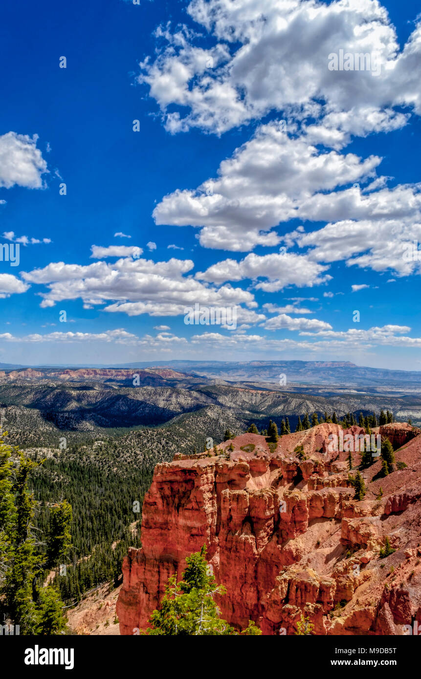 Bild vertikal mit Blick auf rot und orange Sandstein Felsformationen mit grünen Tal unten unter blauen Himmel mit weißen Wolken. Stockfoto