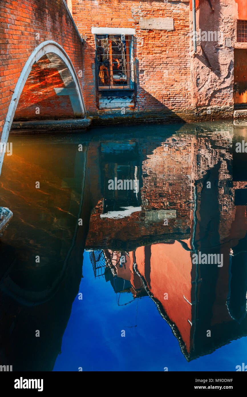 Fenster mit Blick auf die stillen Wasser des Kanals mit Tiefe und klare Reflexion des Gebäudes und der Sonne unter Brücke erzeugen Lichteffekte in Venedig nieder Stockfoto