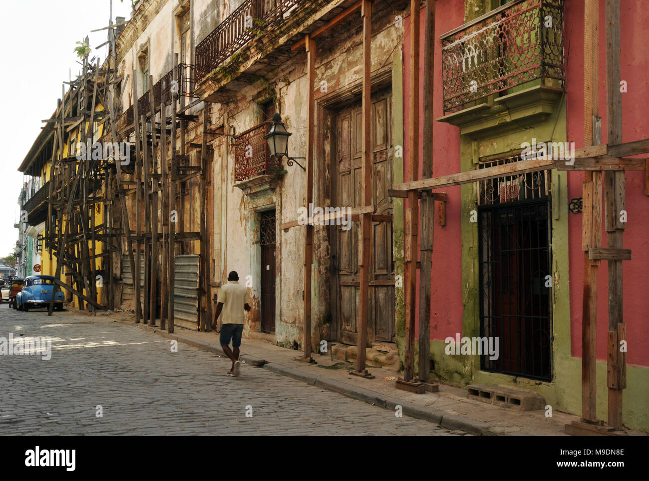 Ein Mann Spaziergänge entlang einer Straße in der Altstadt von Havanna, Kuba, vorbei an alten, unrestaurierten Gebäude mit Balkonen und hölzernen Gerüst befestigt. Stockfoto