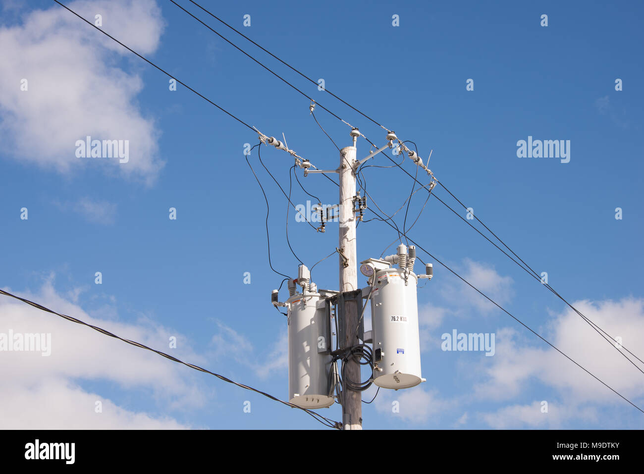 Zwei elektrische Transformatoren auf einer Stange mit Kabeln, Steckern und Isolatoren mit einem tiefblauen Himmel und weißen Wolken Hintergrund. Stockfoto