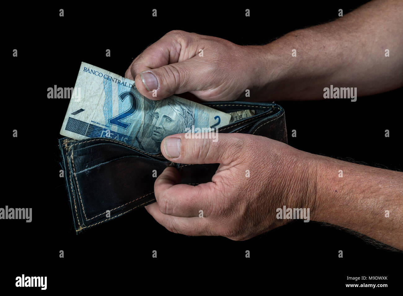Die Hände des Menschen ein Zwei reals Banknote ein Portemonnaie, auf schwarzem Hintergrund Stockfoto