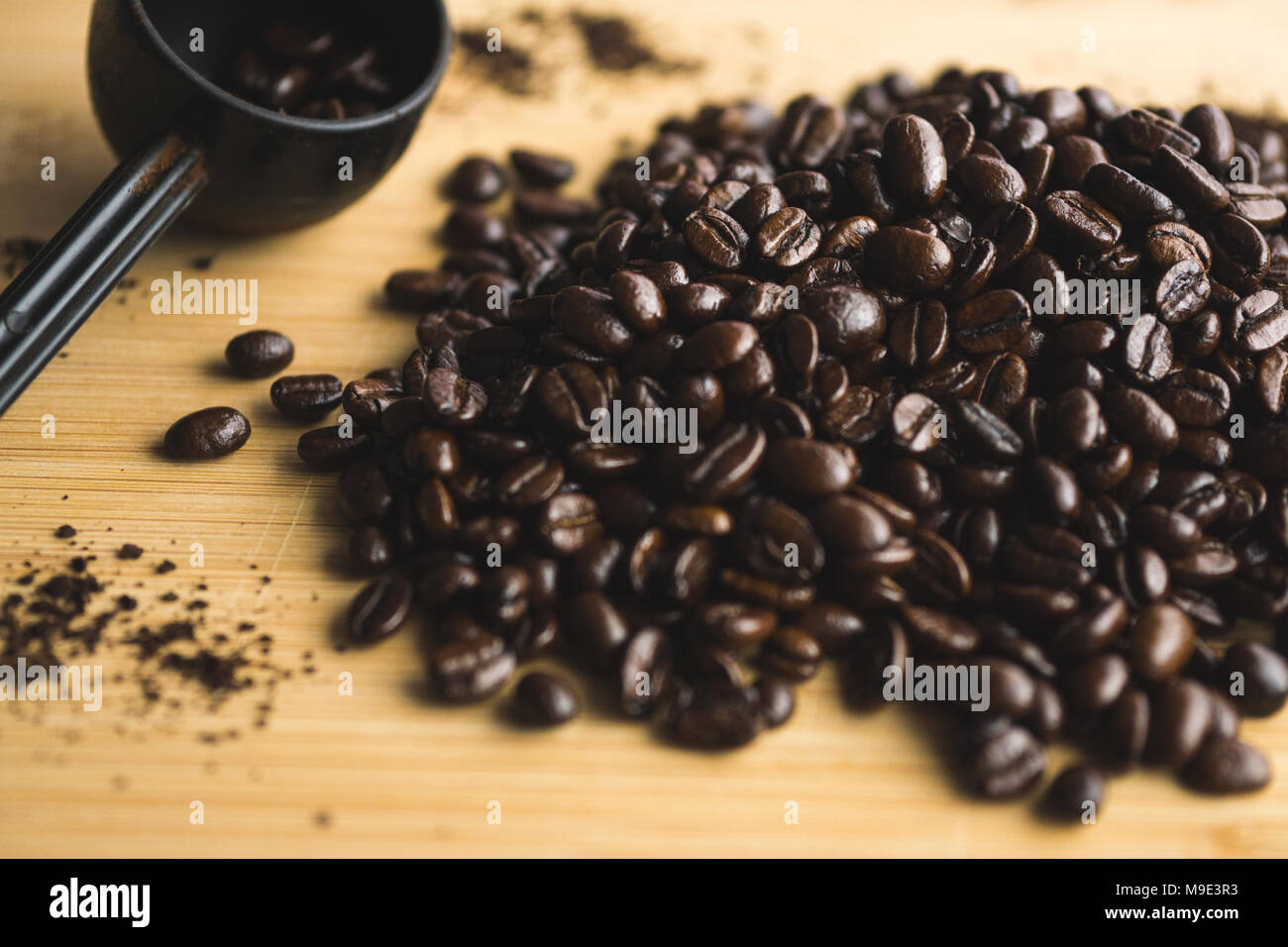 Messlöffel und verschüttete Kaffeebohnen auf Holzbrett. Stockfoto