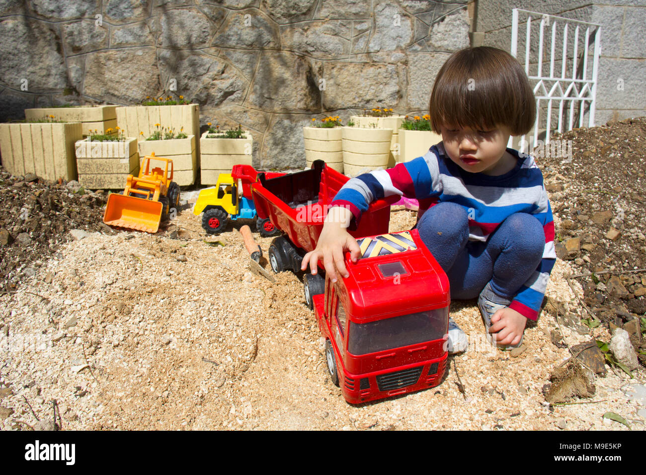 Wenig drei Jahre alten Jungen spielen im Sand mit einem Bagger und Kipper. Stockfoto