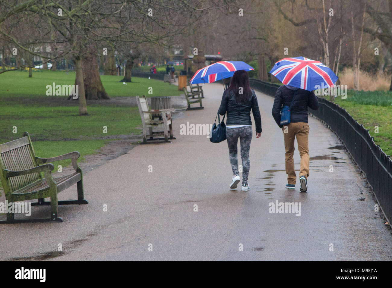 Ein paar Spaziergang durch St. James's Park mit Union Jack Schirme an einem kalten, grauen, nassen Tag in London. Stockfoto