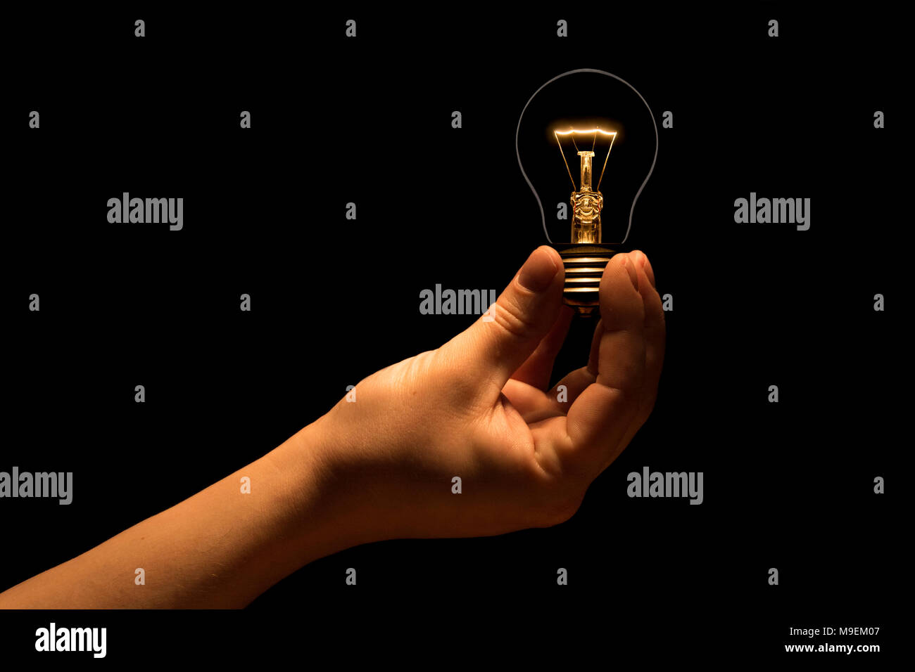 Hand, die eine Glühlampe auf schwarzem Hintergrund. Die Glühbirne als Symbol für eine Idee. Glühende tungsten Birne. Ökologische Konzept. Stockfoto