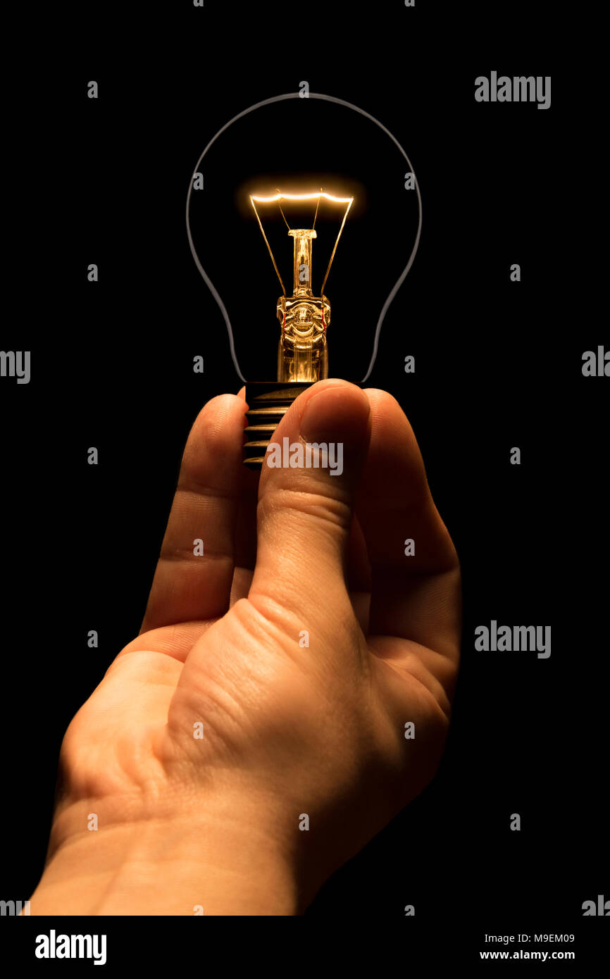 Hand, die eine Glühlampe auf schwarzem Hintergrund. Die Glühbirne als Symbol für eine Idee. Glühende tungsten Birne. Ökologische Konzept. Stockfoto