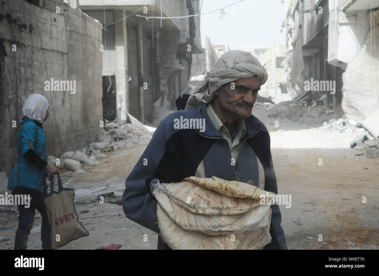 Damaskus. 24 Mär, 2018. Ein Mann hält ein Bündel von Brot, das er von einer Bäckerei, die vor kurzem in der Stadt Ayn Tarma im östlichen Ghuta Landschaft der Hauptstadt Damaskus, Syrien am 24. März 2018 wieder eröffnet. Die Syrische Armee hat über 80 Prozent der Ayn Tarma gefangen, während die Rebellen den Rückzug aus wichtigen Bereichen sind im Osten Ghuta. Credit: Ammar Safarjalani/Xinhua/Alamy leben Nachrichten Stockfoto