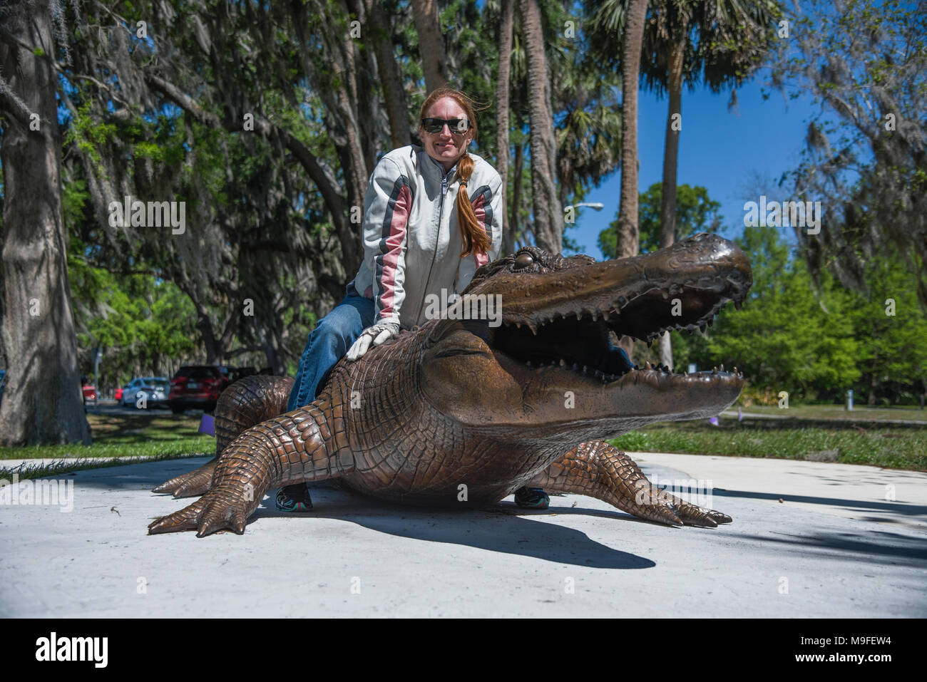 Hübschen roten Kopf Mädchen mit Sonnenbrille mit einem Bronze Alligator Statue posiert Stockfoto