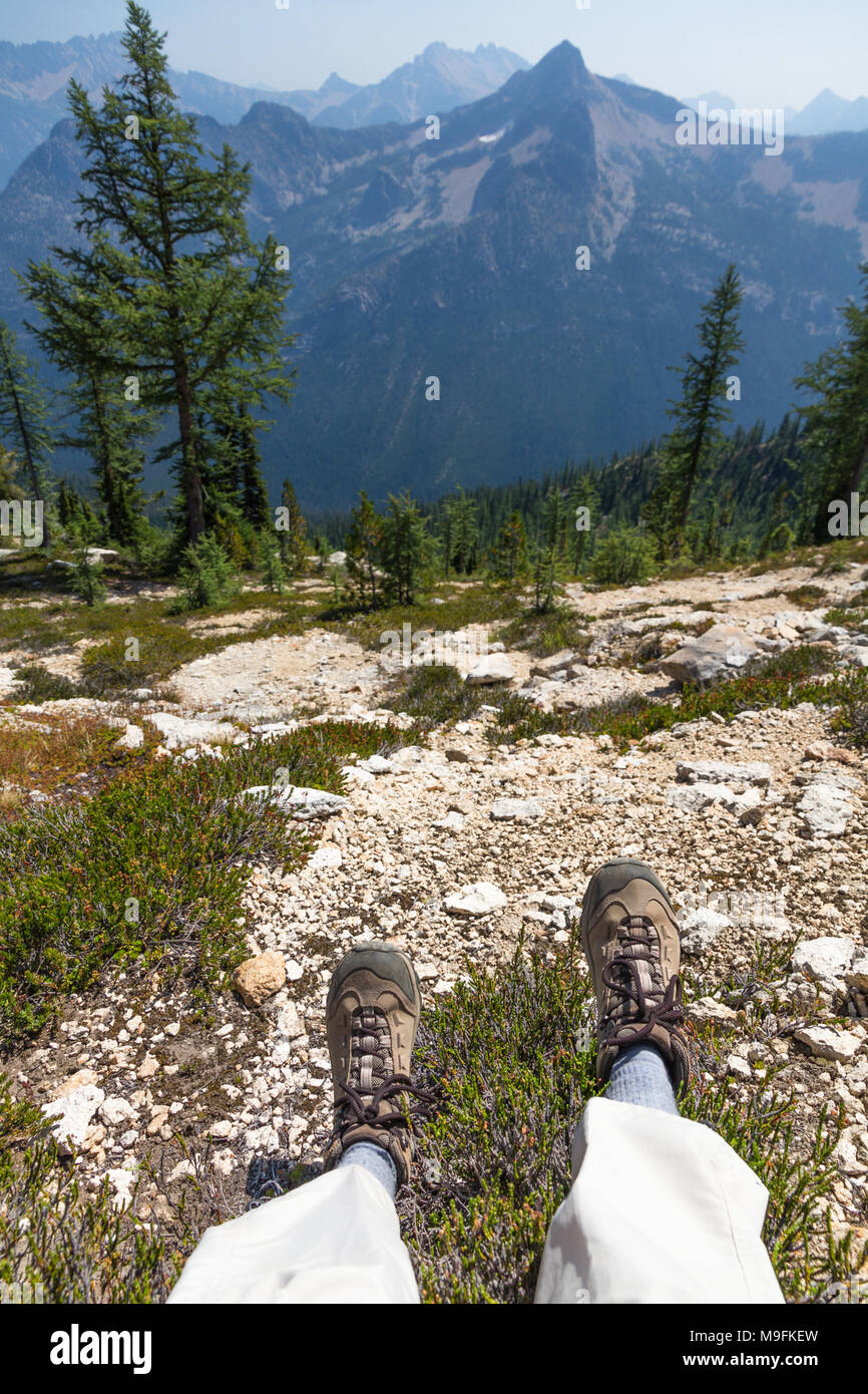 Paar Wanderschuhe zeigen ein Wanderer ruht der Blick hinunter zu genießen, felsigen Hang zu Wald und schroffen Gipfeln North Cascades Stockfoto