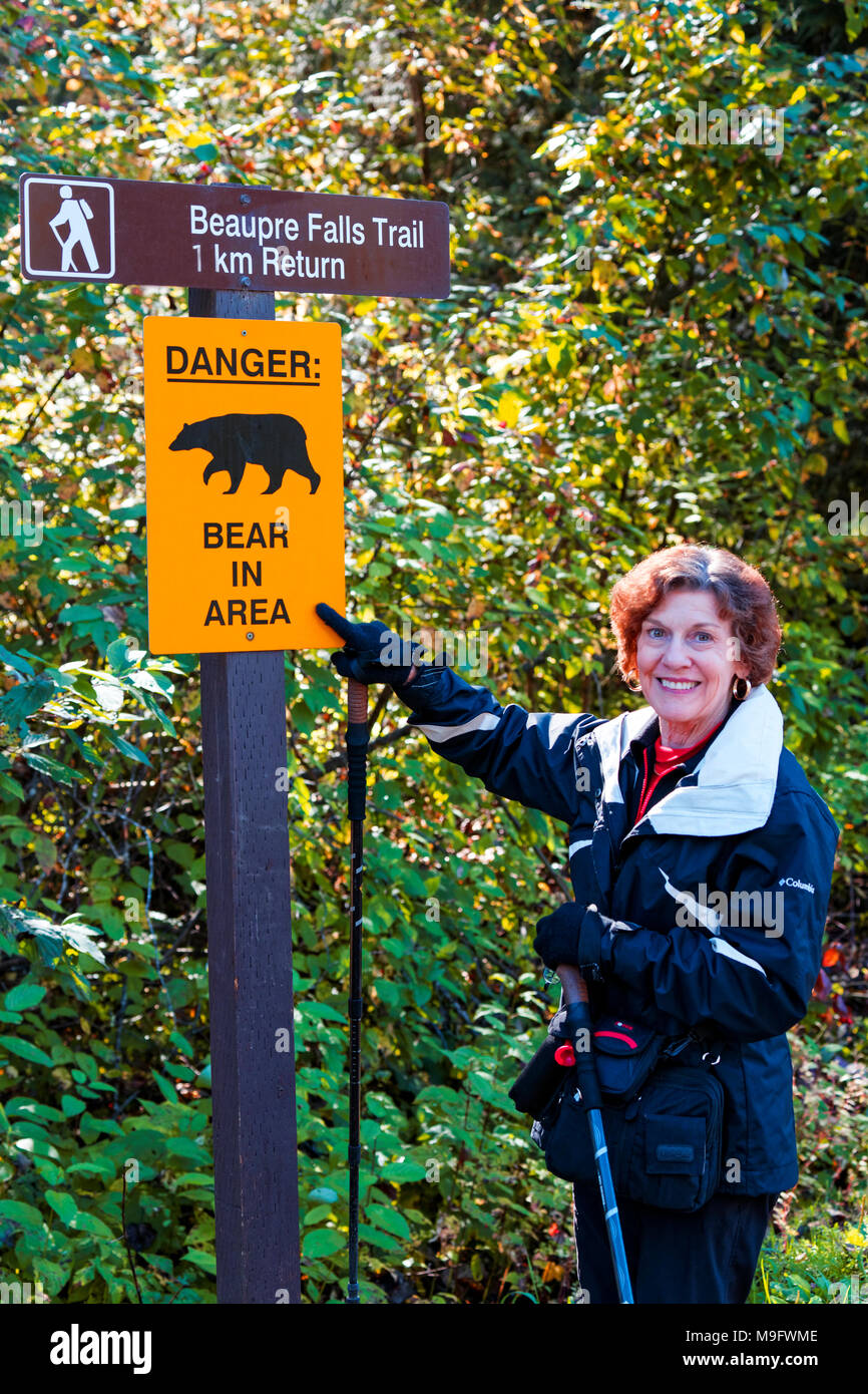 42,633.05745 lächelnde Frau Wanderer stand neben einem Bären Warnschild entlang einer Forststraße Stockfoto