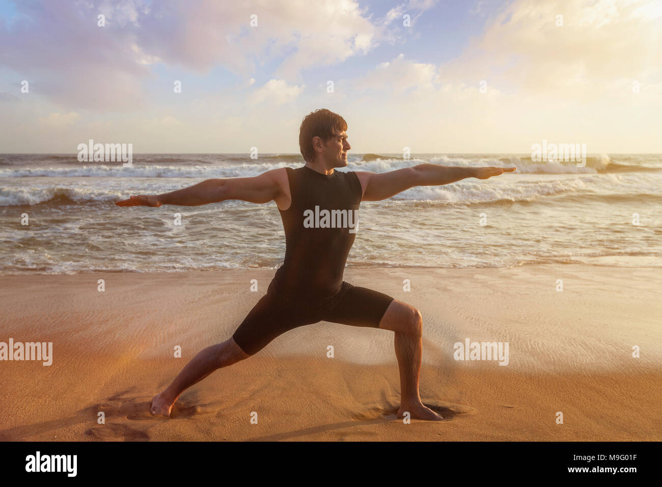 Man Yoga Asana Virabhadrasana 1 Warrior Pose am Strand Stockfoto